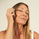 Mature woman applying Eyelash Enhancing Serum on her right eyelashes