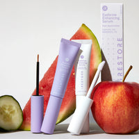 Eyelash Enhancing Serum and Eyebrow Enhancing Serum beside each other with fruits and packaging behind