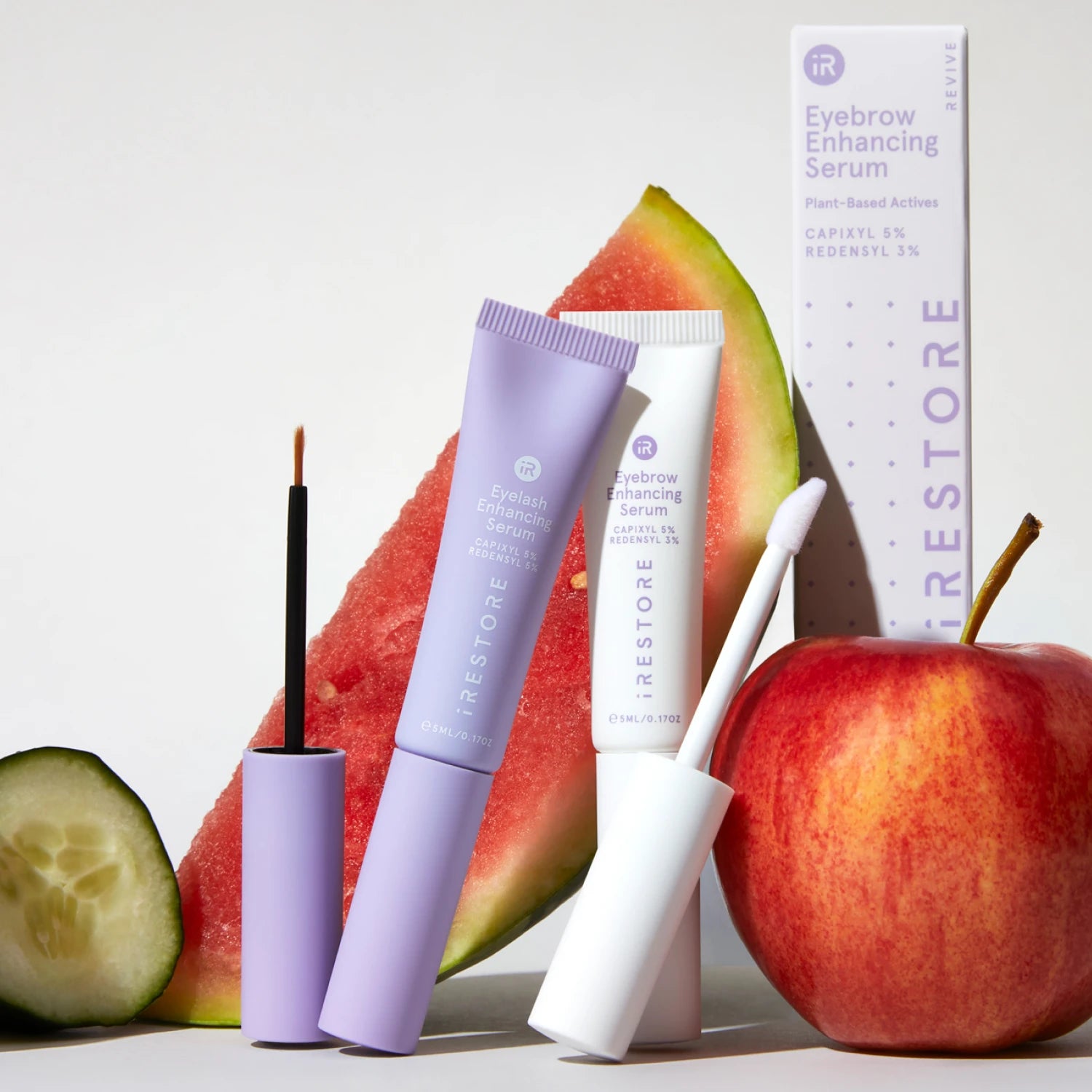 Eyelash Enhancing Serum and Eyebrow Enhancing Serum beside each other with fruits and packaging behind