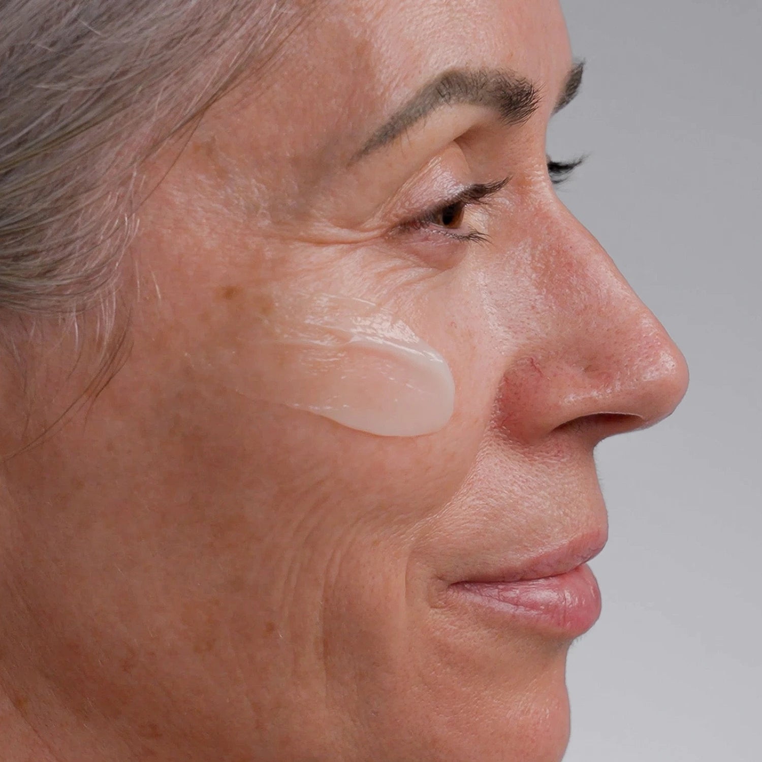 Close-up of a woman's face with Advanced Retinol Serum application on her cheek against a neutral background