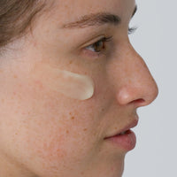 Close-up of a woman's face with Vitaminc C Serum applied on her cheek against a neutral background