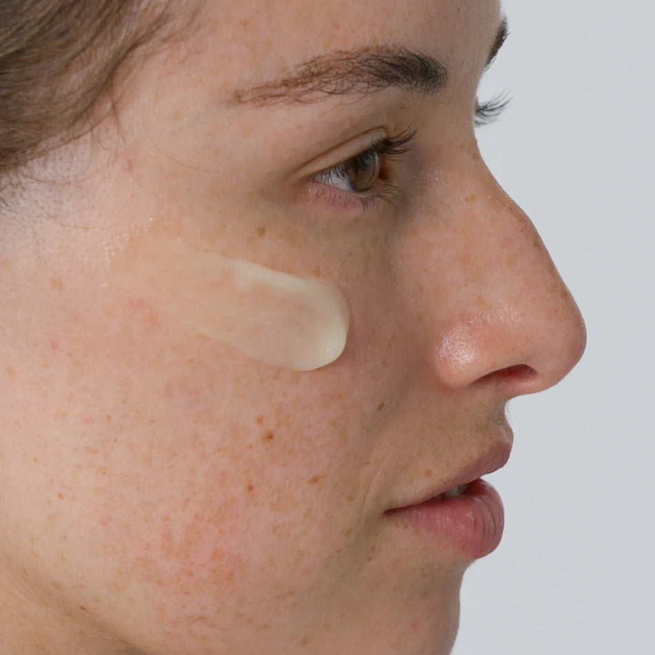 Close-up of a woman's face with Vitaminc C Serum applied on her cheek against a neutral background