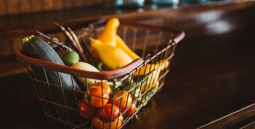 Fruits and vegetables inside a steel basket on top of wooden table.