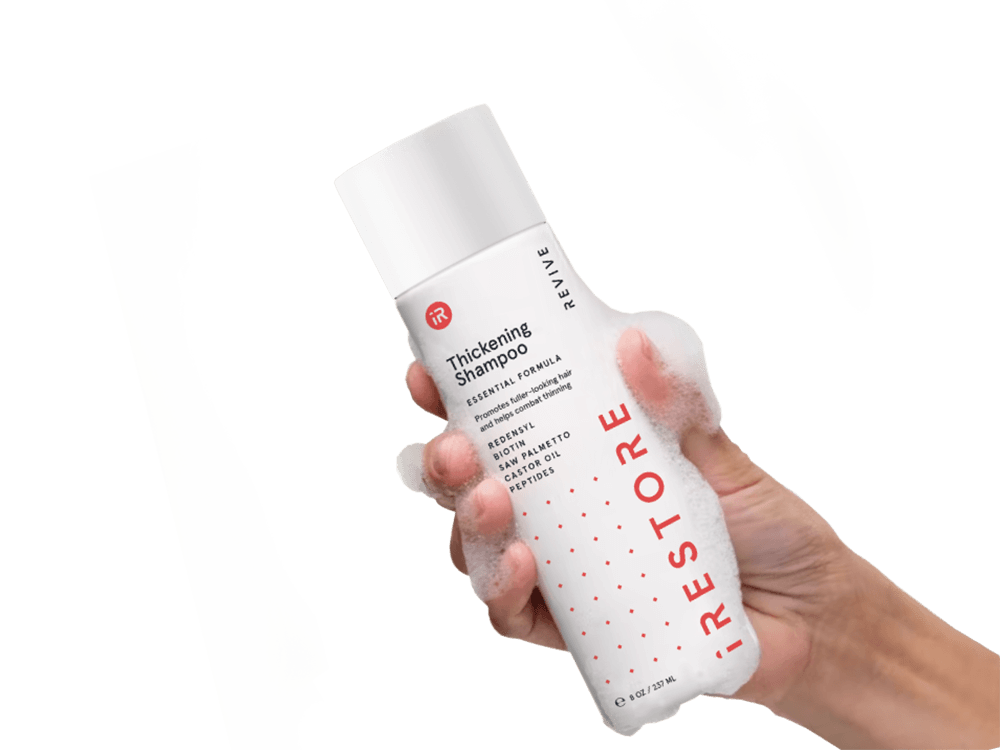 Image of a hand holding the Thickening Shampoo with bubbles all over the hand and bottle.