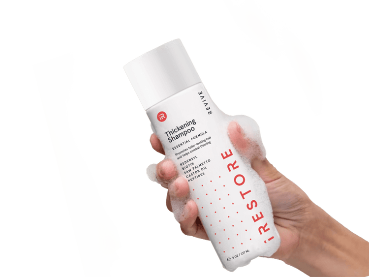 Image of a hand holding the Thickening Shampoo with bubbles all over the hand and bottle.