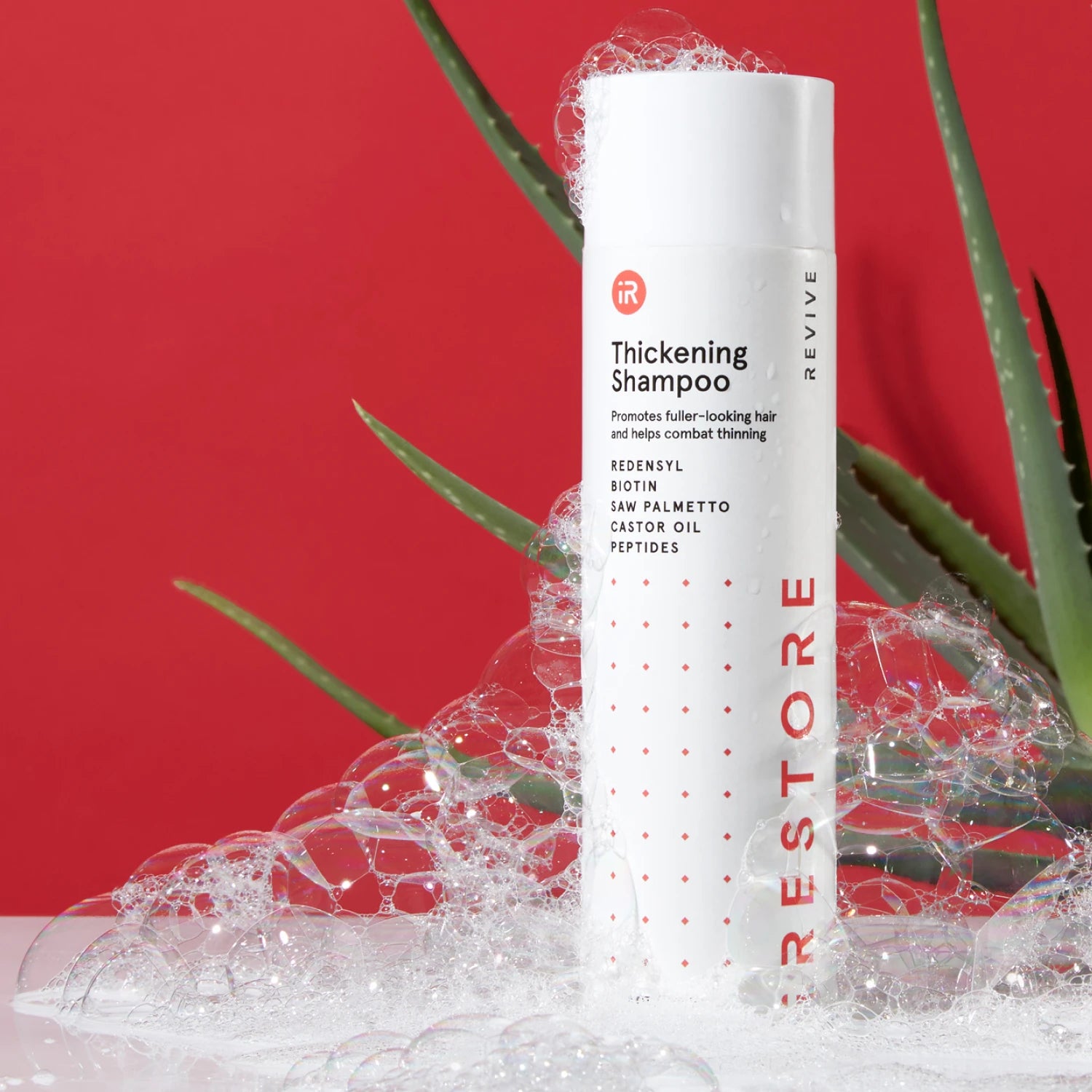 Image showing the Thickening Shampoo placed on top of a table with bubbles all over the bottle and showing an aloe vera behind the bottle.