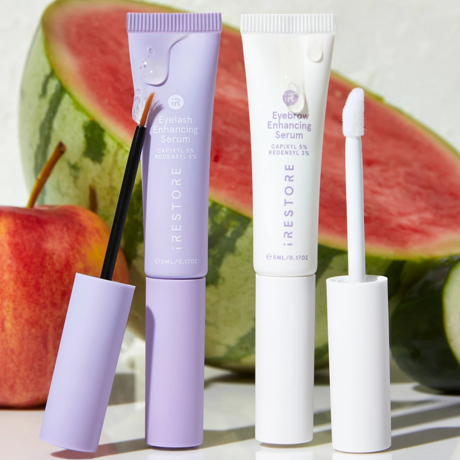 Image of the Eyebrow and Eyelash Enhancing Serum with the applicator beside each other showing apple and watermelon in the background.
