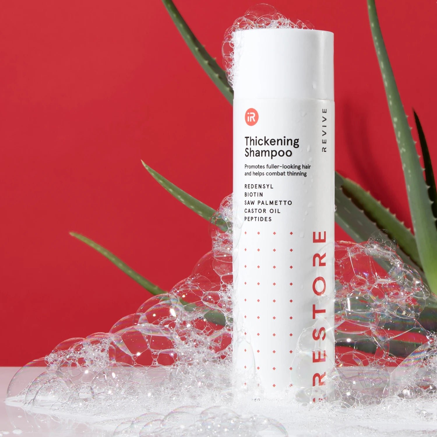 Image showing the Thickening Shampoo placed on top of a table with bubbles all over the bottle and showing an aloe vera behind the bottle.