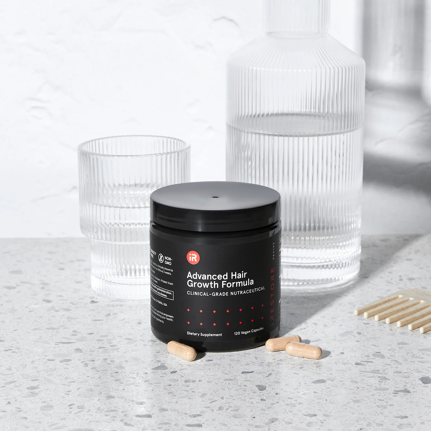 Black jar of Advanced Hair Growth Formula capsules with water glasses in the background.