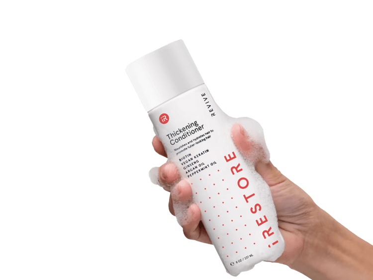 Image of a hand holding the Thickening Conditioner with bubbles all over the hand and bottle.