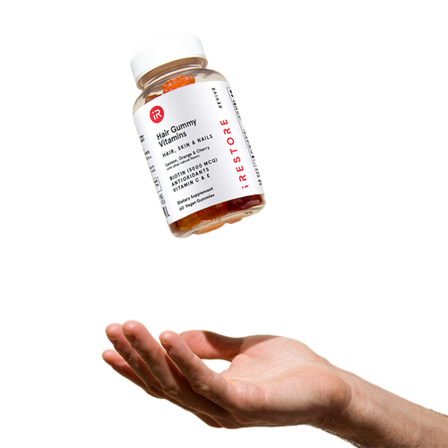 Biotin gummies bottle in mid air with a hand below to catch it.
