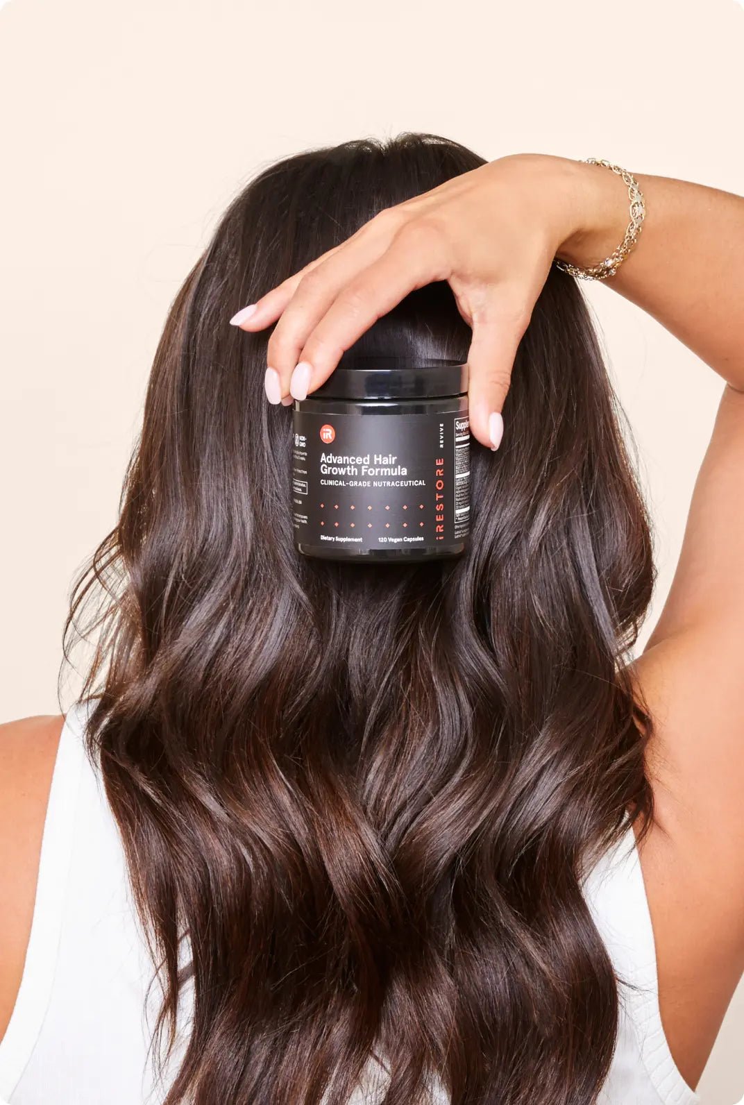 Image of a woman with long, wavy brown hair holds a jar the  Advanced Hair Growth Formula above her head, showcasing the product's on hair growth.