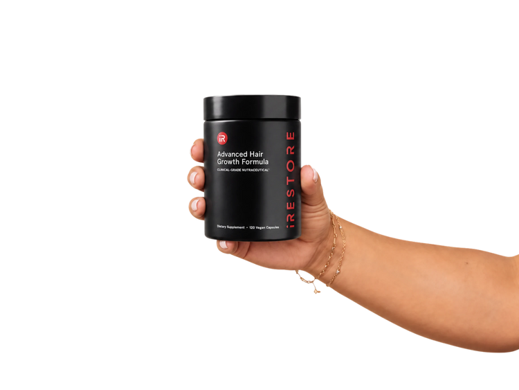 A hand holding a black jar of iRestore Advanced Hair Growth Formula against a solid white background.