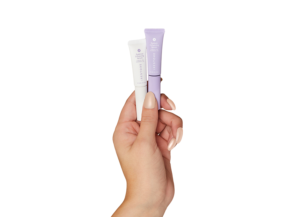 Hand holding eyelash enhancing serum and eyebrow enhancing serum