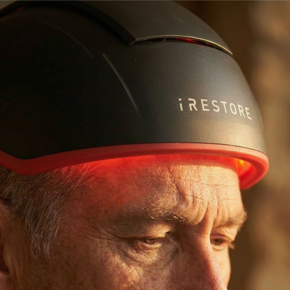 Person wearing a black device labeled 'iRESTORE' on their head with a blurred background.