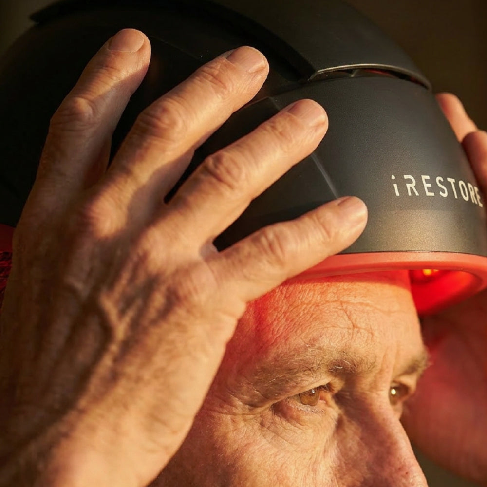 Person using a device labeled 'iRESTORE' on their head with a warm glow.