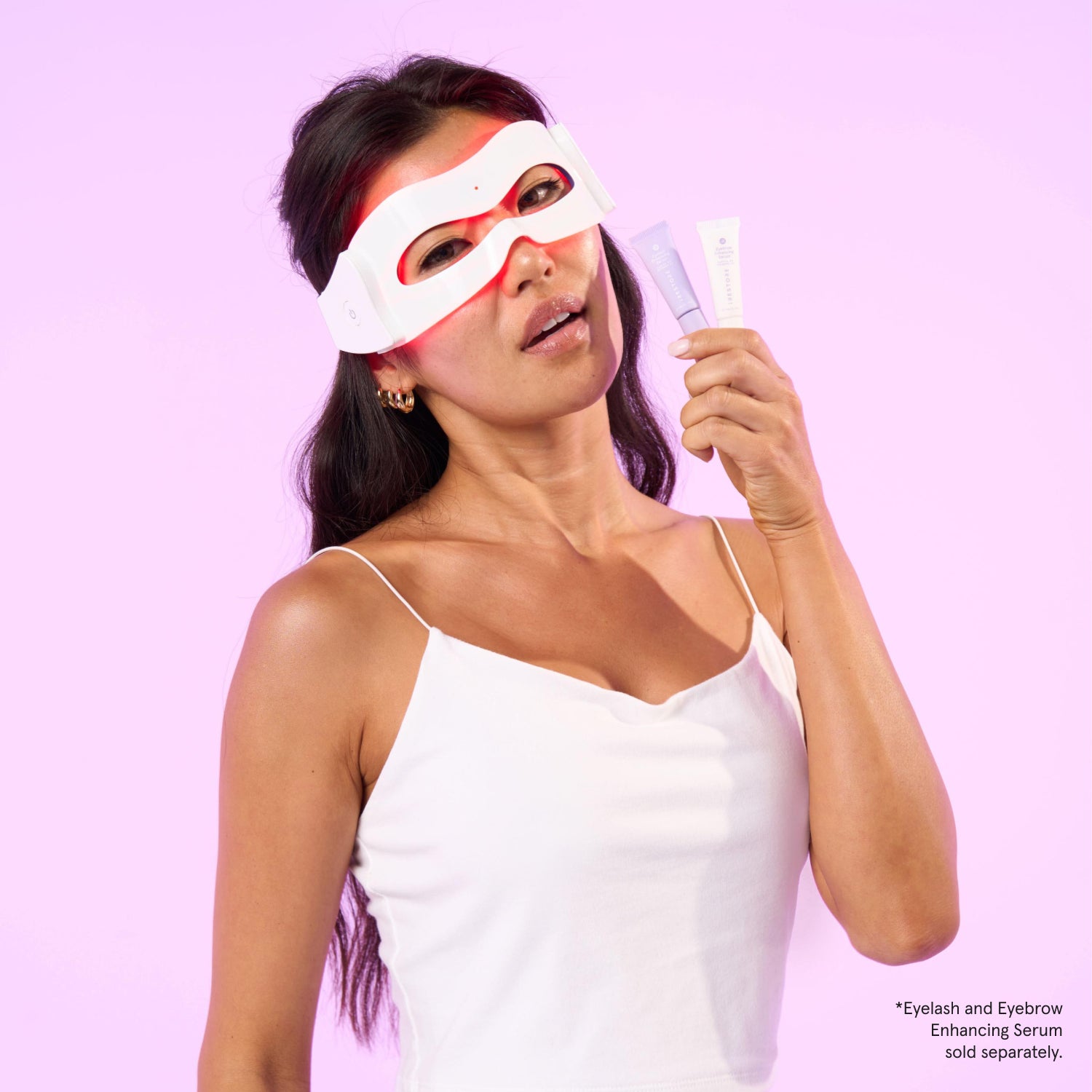 Woman wearing  the LED eye mas while holding Eyelash and Eyebrow enhancing serum