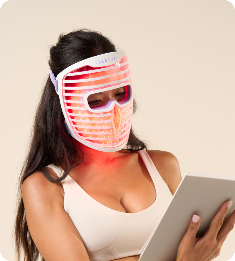 Woman wearing the iRESTORE LED face mask while reading a book