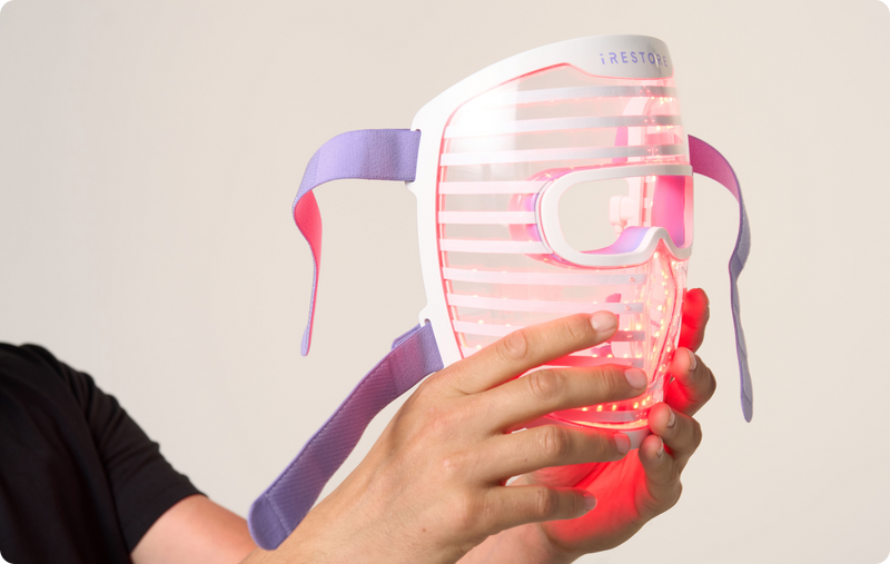 Close up shot of hands holding the LED face mask with red light turned on