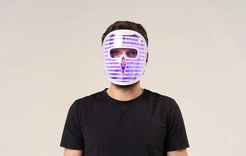 Man in black shirt wearing the iRESTORE LED face mask with blue light turned on