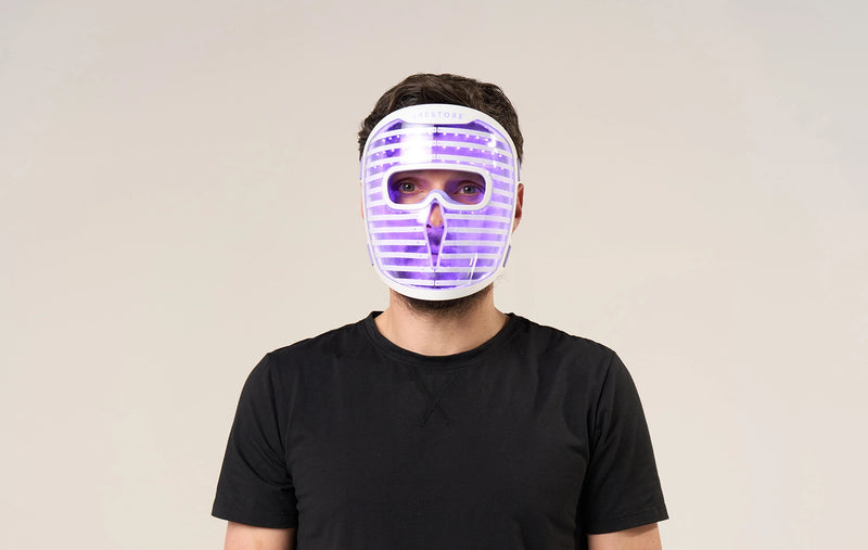 Man in black shirt wearing the iRESTORE LED face mask with blue light turned on