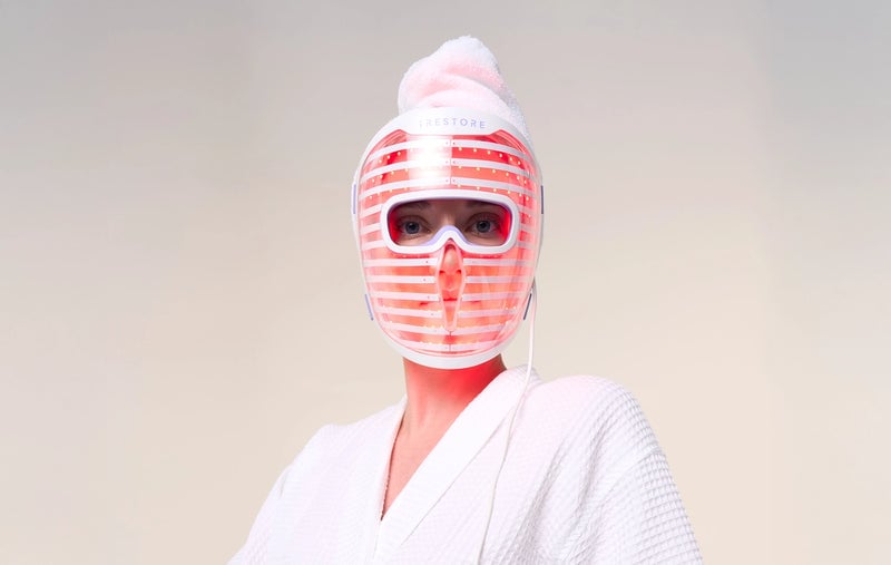 Woman in bathrobe wearing the iRESTORE LED face mask with red light turned on