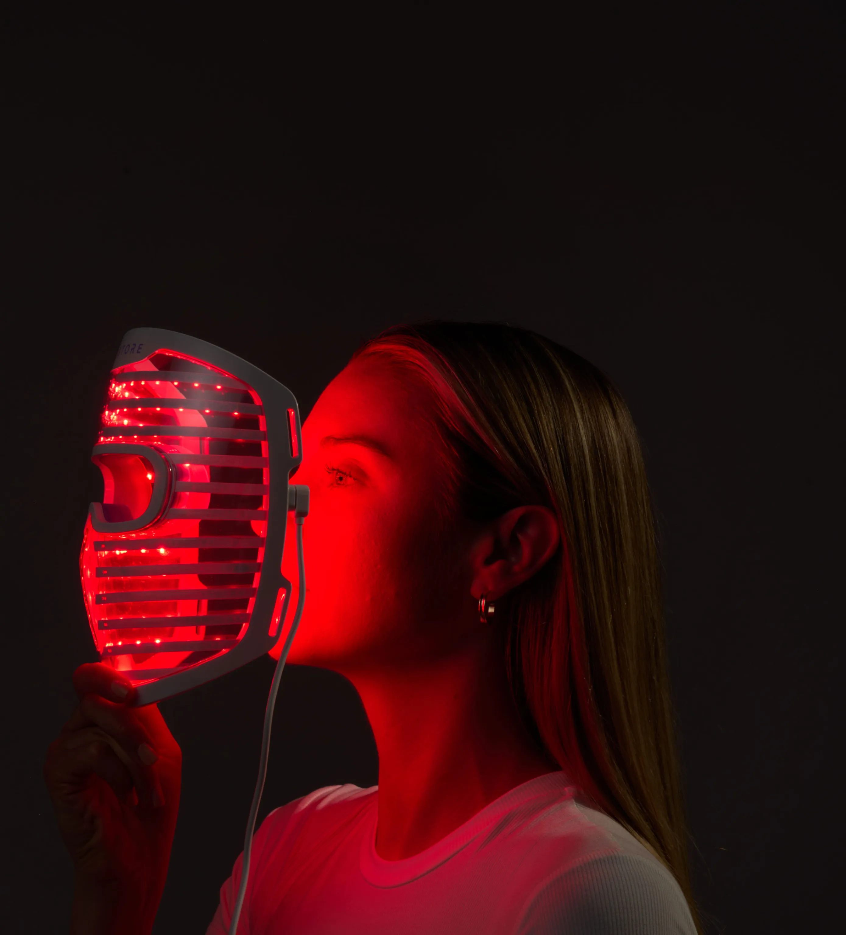 Image of a woman holding the Illumina Face Mask with its lights on, right in front of her face.