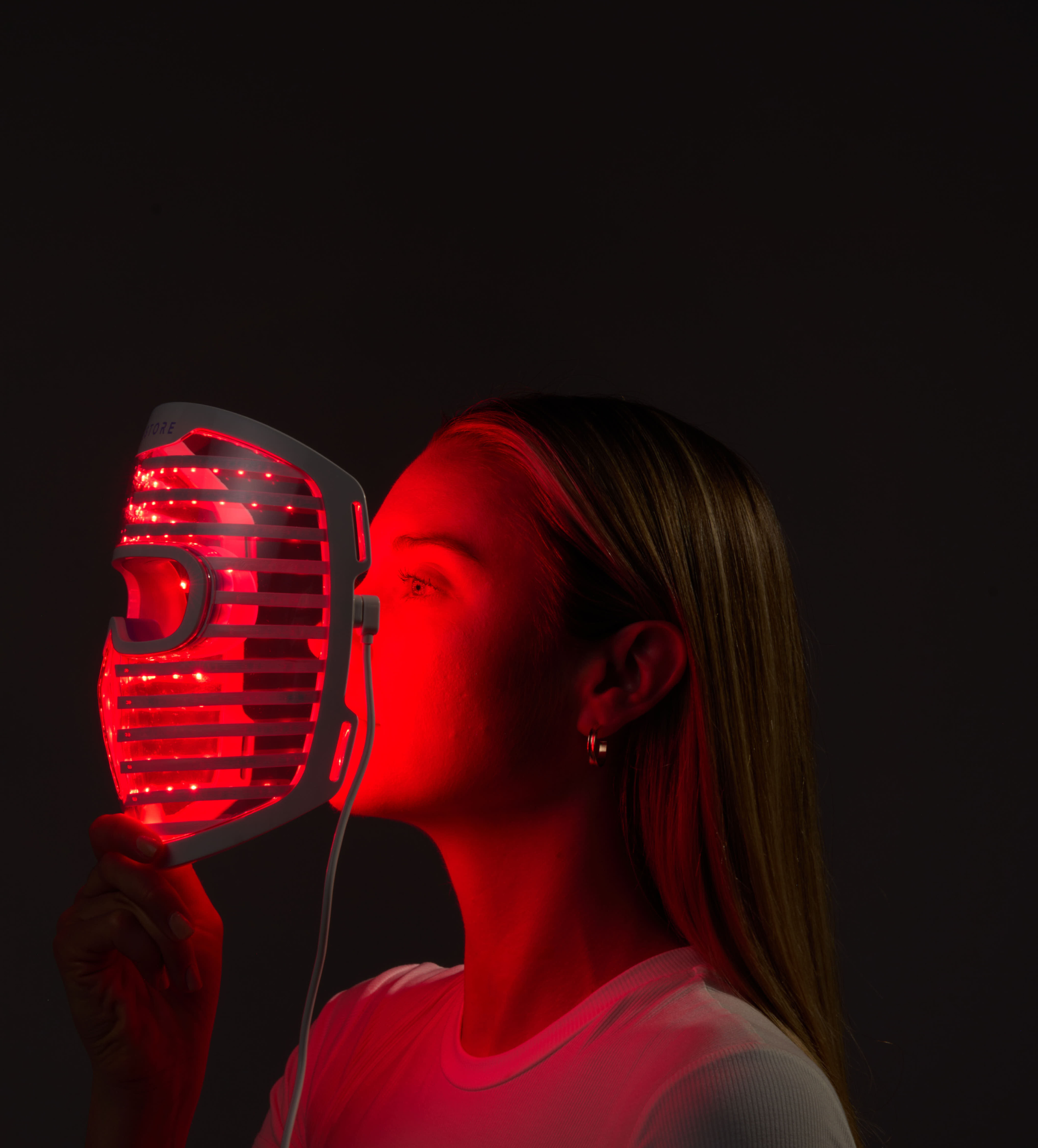 Image of a woman holding the Illumina Face Mask with its lights on, right in front of her face.