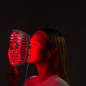 Image of a woman holding the Illumina Face Mask with its lights on, right in front of her face.