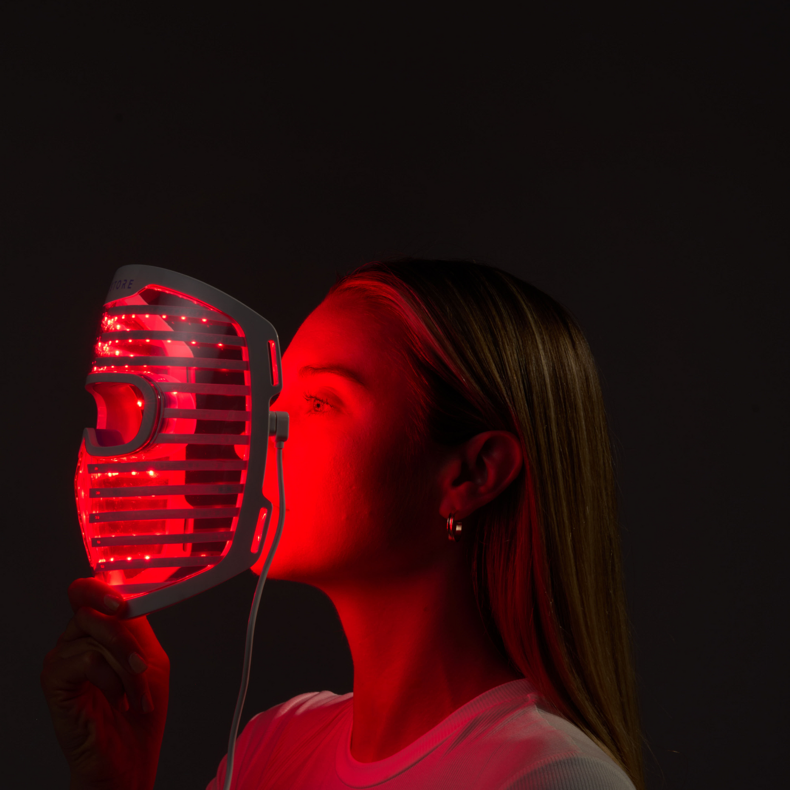 Image of a woman holding the Illumina Face Mask with its lights on, right in front of her face.