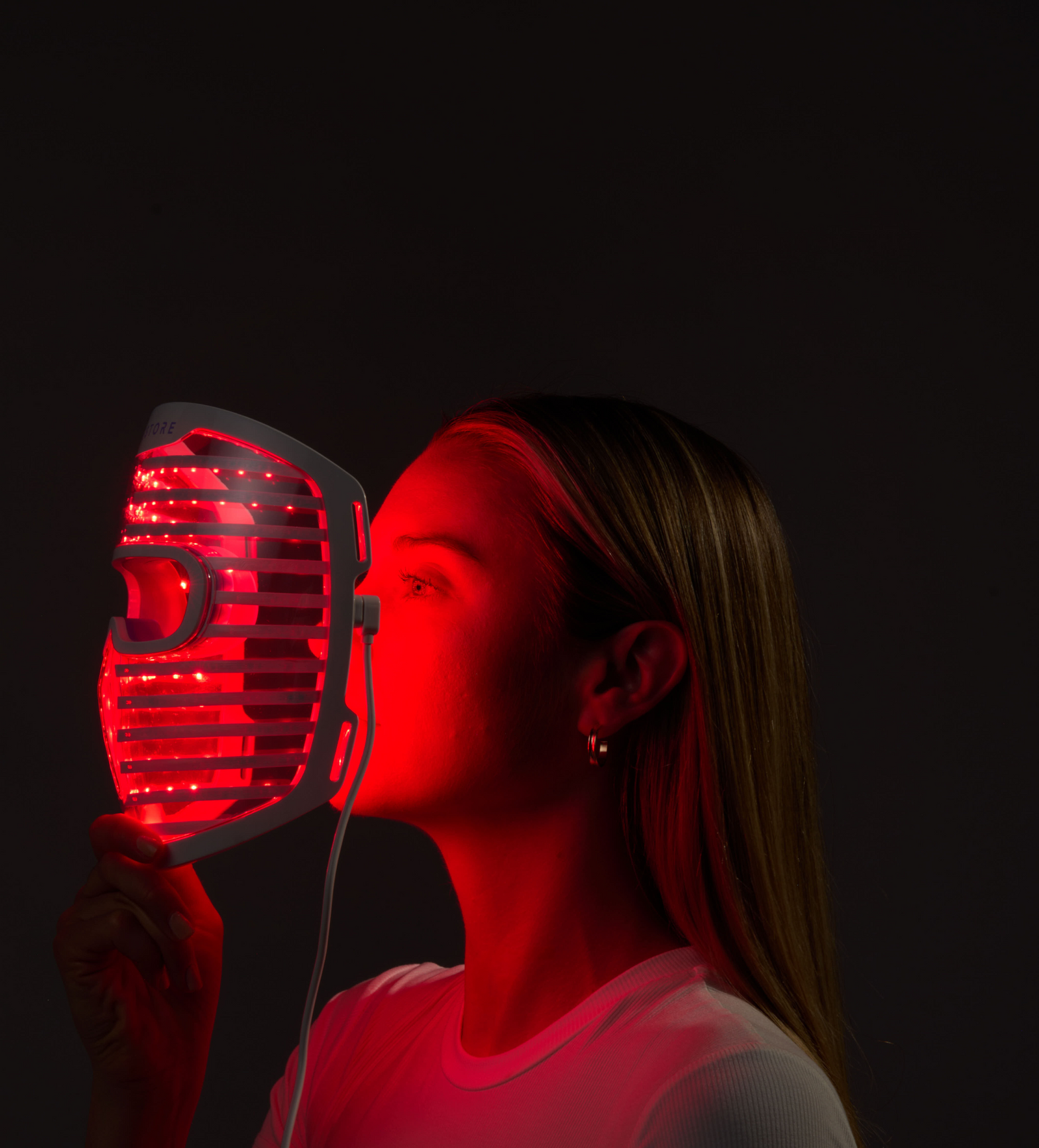 Image of a woman holding the Illumina Face Mask with its lights on, right in front of her face.