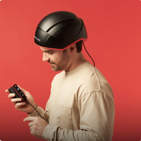 Image of a man wearing the Elite device while holding the battery pack connected to the helmet. device.