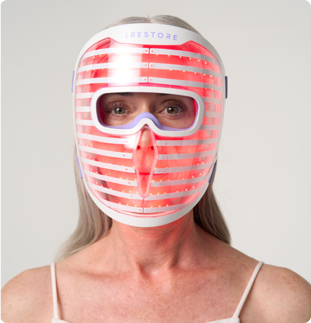 Mature woman wearing the iRESTORE LED face mask with red light turned on
