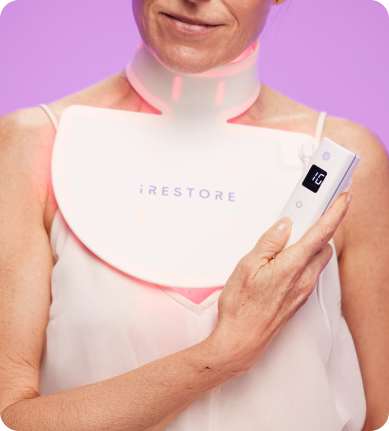 Mature woman holding the device remote while wearing the iRESTORE led neck and chest mask