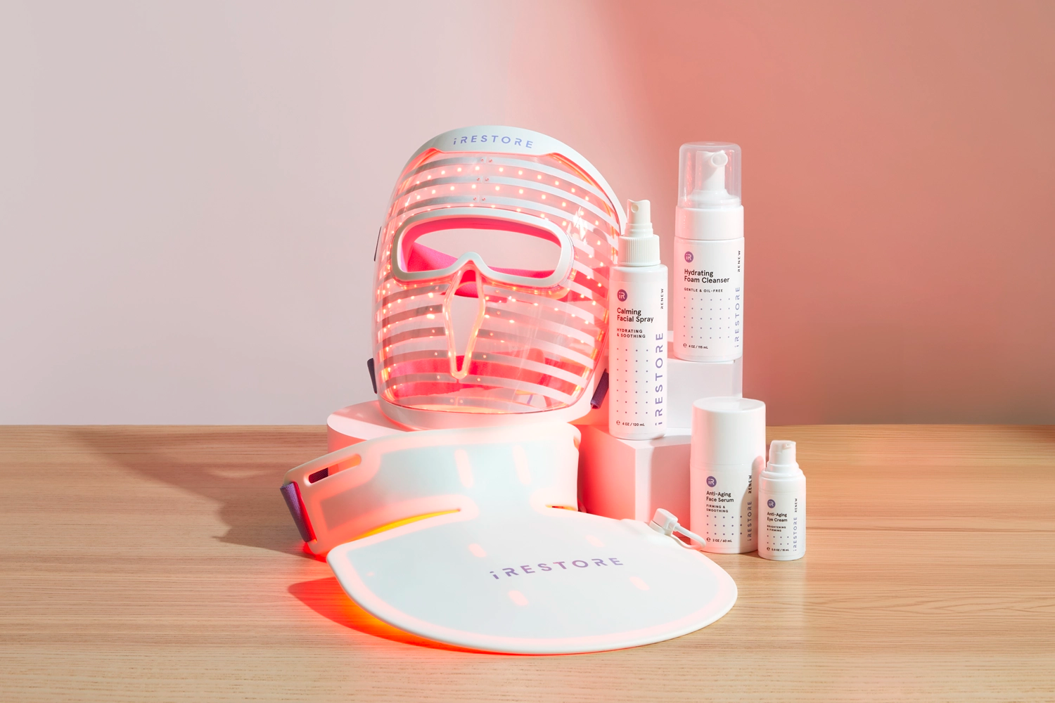 LED face mask, LED neck and chest mask, Calming facial spray, Hydrating foam cleanser, Anti-aging face serum, and Anti-aging eye cream on top of a wooden table