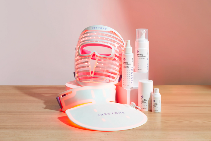 LED face mask, LED neck and chest mask, Calming facial spray, Hydrating foam cleanser, Anti-aging face serum, and Anti-aging eye cream on top of a wooden table