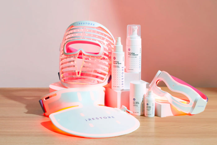 LED face mask, LED neck and chest mask, LED eye mask, Calming facial spray, Hydrating foam cleanser, Anti-aging face serum, and Anti-aging eye cream on top of a wooden table