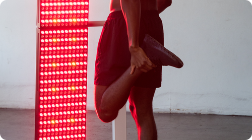 Man stretching in front of a glowing red and amber LED therapy panel