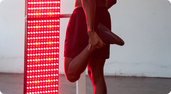 Man stretching in front of a glowing red and amber LED therapy panel