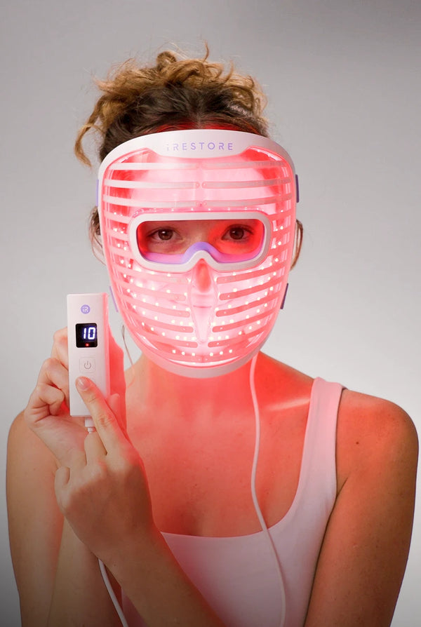 Person wearing a LED face mask with visible control device on a gray background