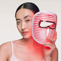 A woman holding the red-glowing Face Mask Pro next to her face.