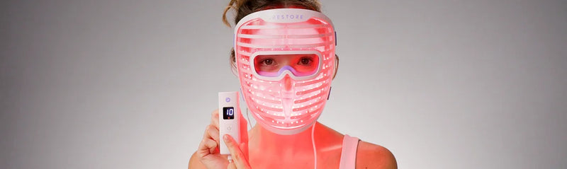 Person wearing a LED face mask with visible control device on a gray background