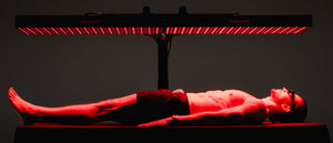 Person lying under a red light therapy panel on a dark background
