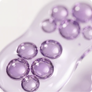 translucent purple liquid droplets and spheres resting inside a clear, gel-like skincare formula.