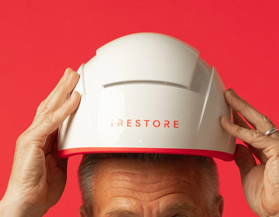 Person holding an iRESTORE Pro above their head against a red background