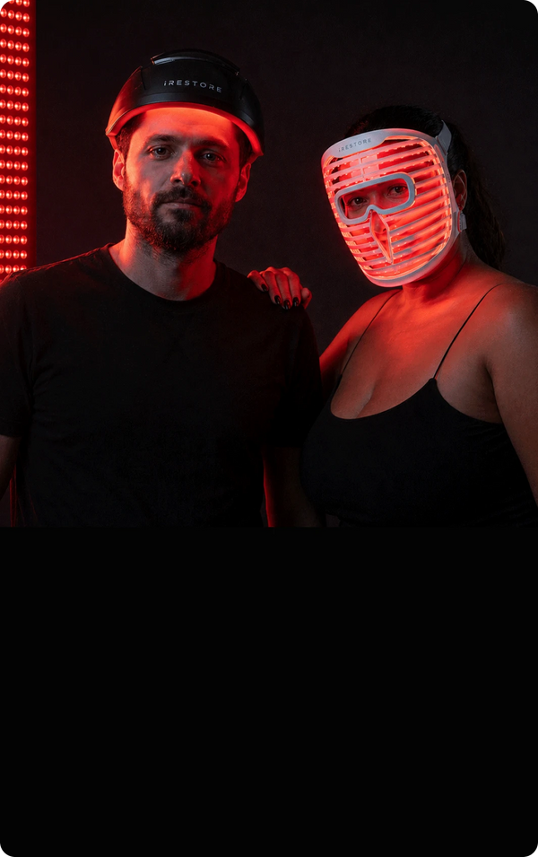Two people posing together with one wearing a LED mask in a red-lit setting.