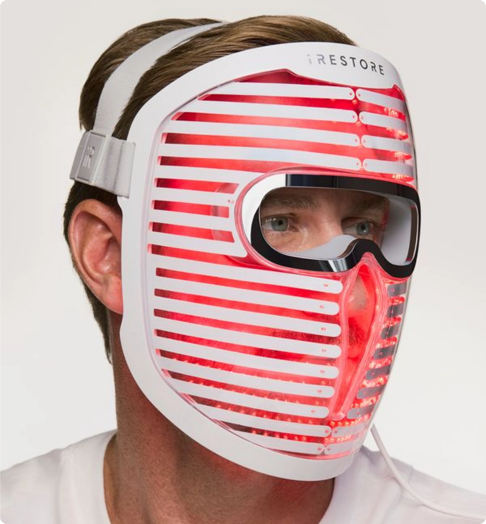 man wearing the iRESTORE Face Mask Pro emitting red light therapy, featuring built-in protective eye goggles and adjustable head straps.