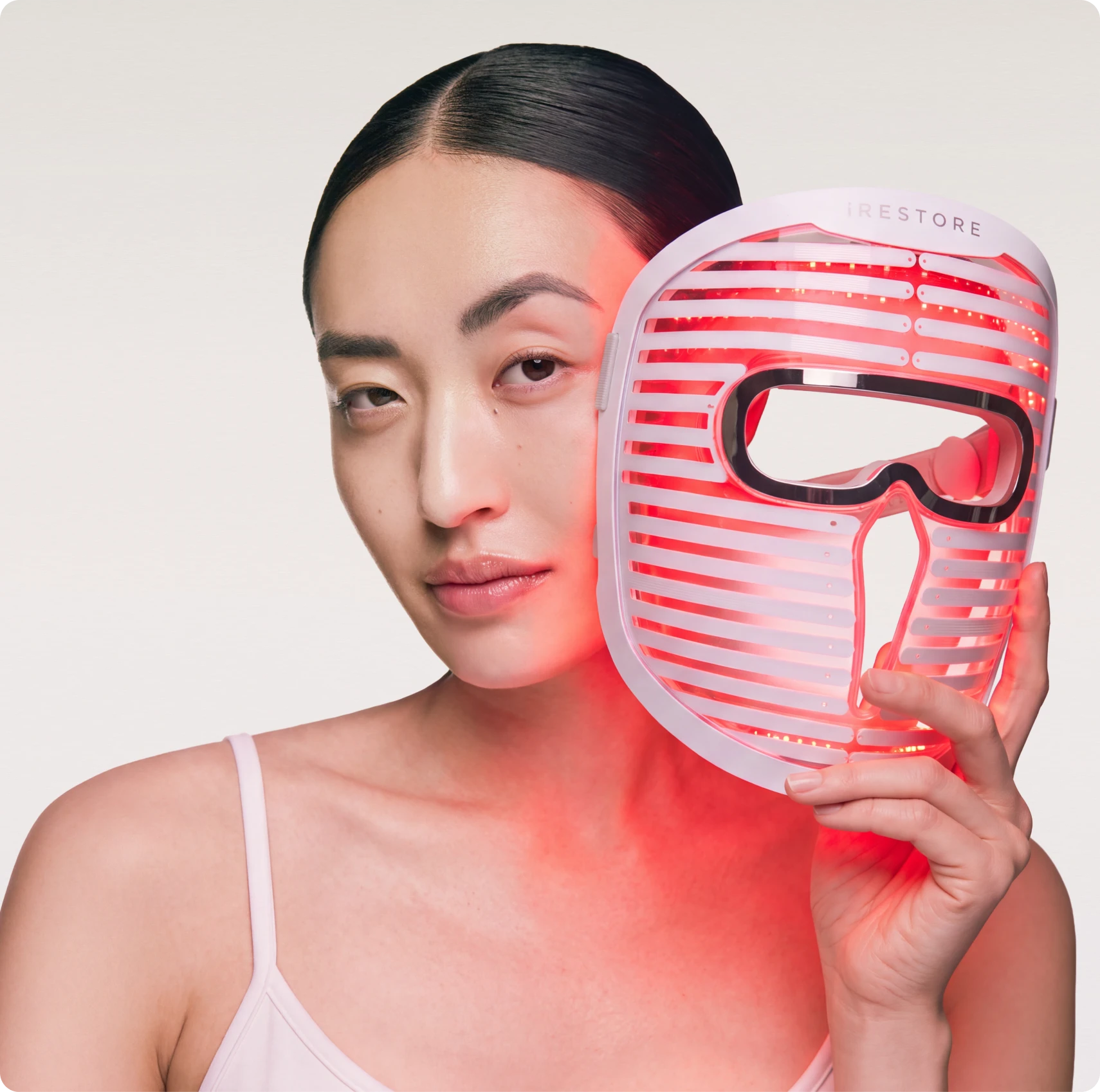A woman holding the red-glowing Face Mask Pro next to her face.