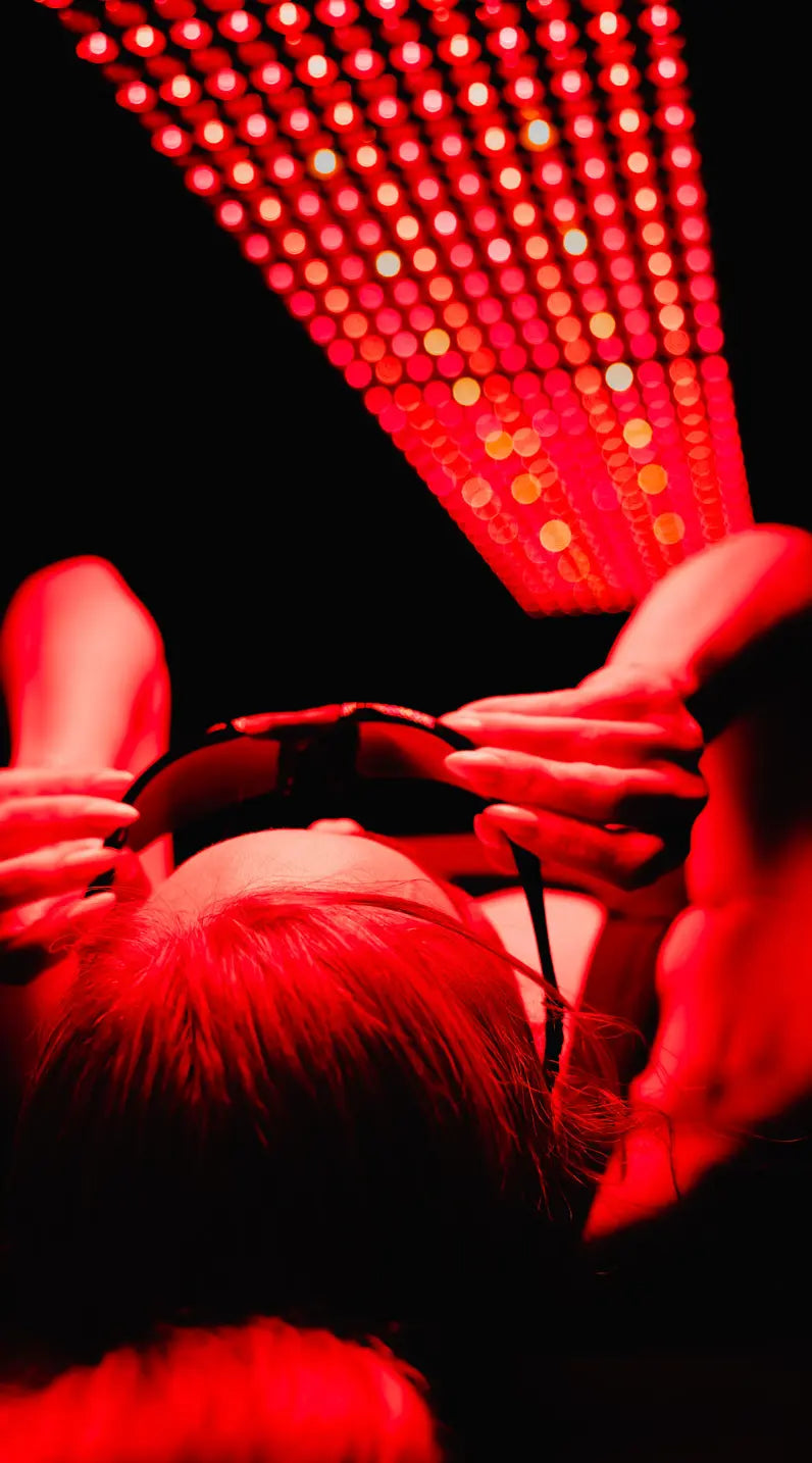 A person wearing Apex VisionGuard protective goggles while lying under a red light therapy panel