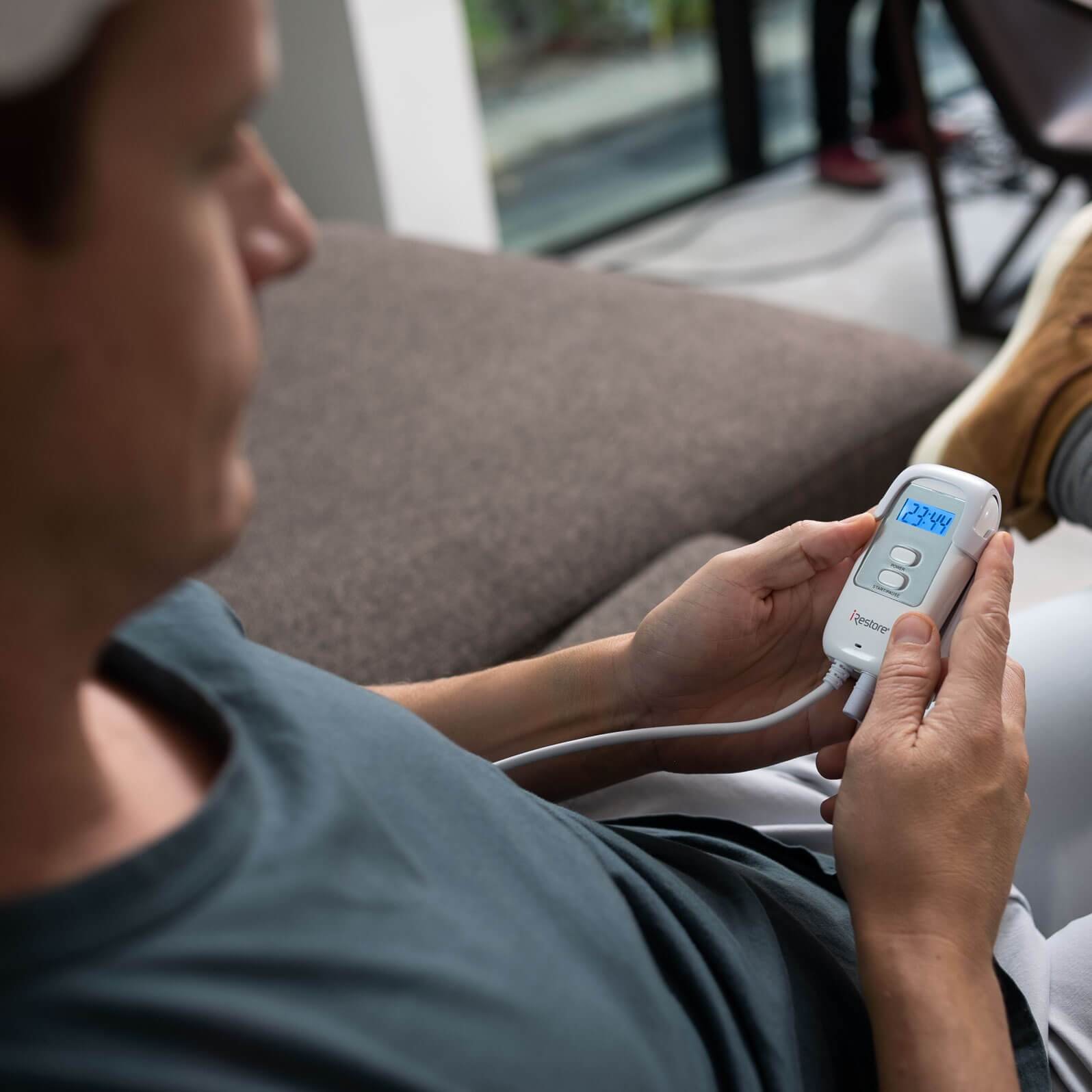 top side view of man wearing the essential device while sitting on a couch. He can be seen holding the device controller.